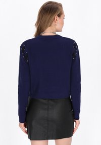 Maglione blu navy accorciato con una lavorazione a maglia testurizzata, con dettagli in pizzo sulle spalle. Abbinato a una gonna in pelle nera aderente.