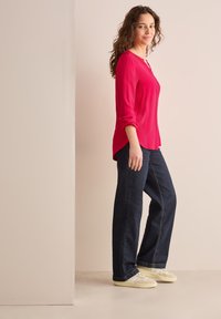 Röd långärmad topp med rund nacke och uppvikta �ärmar, kombinerad med mörkblå vida jeans och ljusa sneakers.