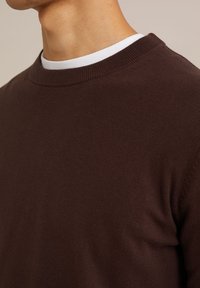 Suéter de punto marrón con cuello redondo. Textura suave y detalles acanalados en el cuello. Tejido ligero adecuado para superponer.