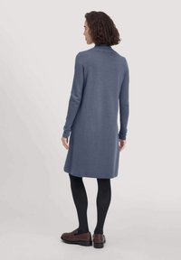 Langarmige, aansluitende jurk in een zachte blauwe stof, met een ronde halslijn en een rechte snit die boven de knie valt, gecombineerd met zwarte panty’s.