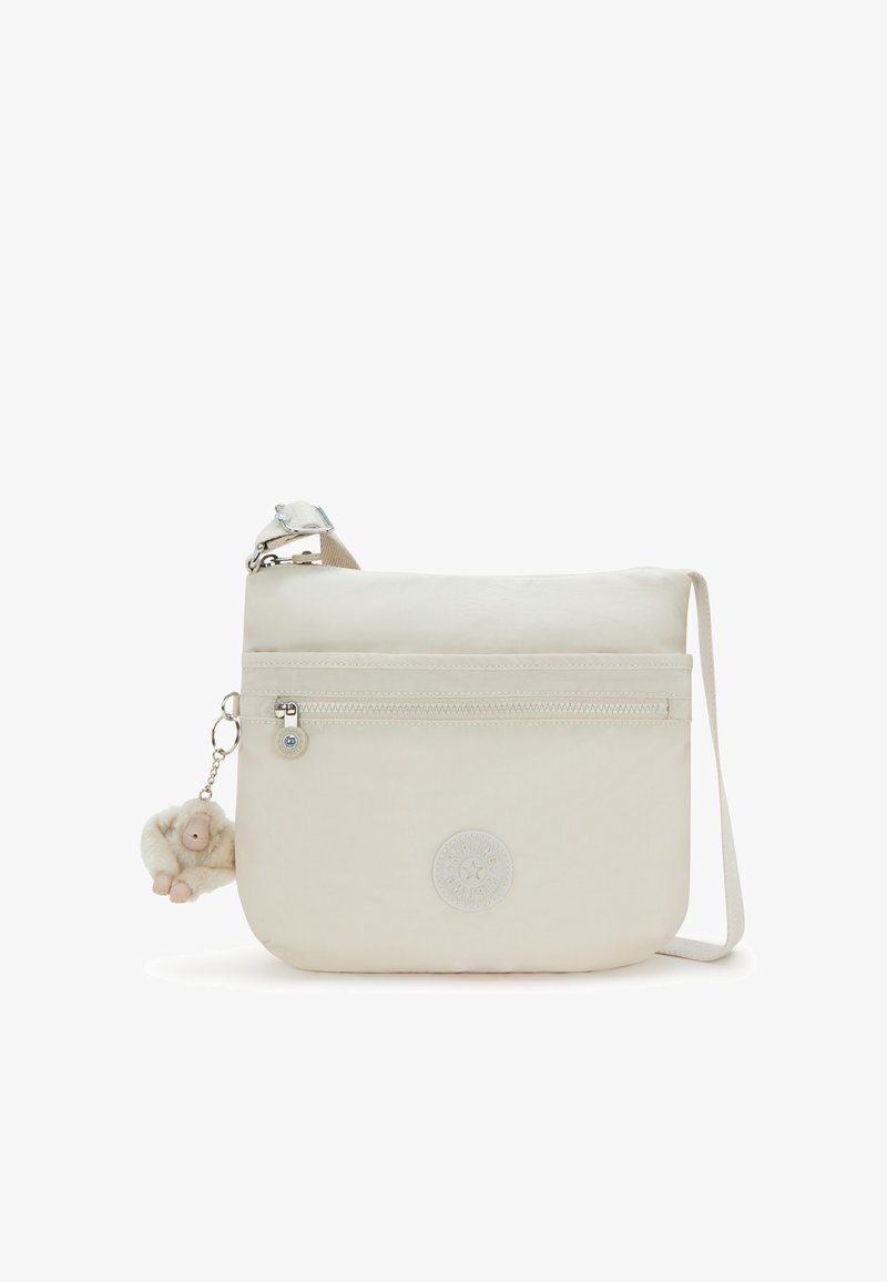 Světlý béžový crossbody vak vyrobený z textilie, se zipovou kapsou na přední straně, logem a odnímatelným plyšovým šimpanzem jako přívěskem.
