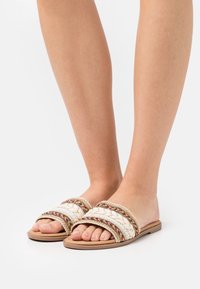 Stickade platta sandaler med beige remmar, med flerfärgade accenter och en strukturerad design. Slät sula och öppen tå-stil.