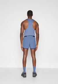 Μπλε αθλητική αμάνικη μπλούζα με σχέδιο racerback, συνδυασμένη με αντίστοιχα σορτς. Διαθέτει λεία υφή και ελάχιστα σχεδιαστικά στοιχεία.