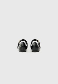 Ballerine nere in pelle con punta arrotondata e tacco basso. Presentano una cinghia regolabile con accessori in tonalità oro e una finitura liscia.