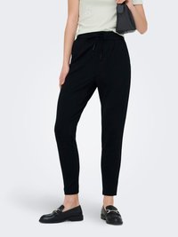 Black tapered pants feature a drawstring waist, soft fabric, and a sleek silhouette. Paired with a light green top and black loafers.