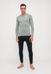 Camisola térmica de mangas compridas em tecido acanelado verde claro, combinada com calças justas pretas, ambas feitas de materiais elásticos.