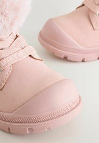 Różowe zimowe buty z grubą gumową podeszwą i sznurowadłami, z futrzanym wykończeniem wokół kostki.