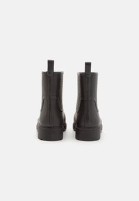 Botines negros de cuero con un panel trasero texturizado, tiradores y suelas de goma, con un acabado liso y diseño clásico chelsea.