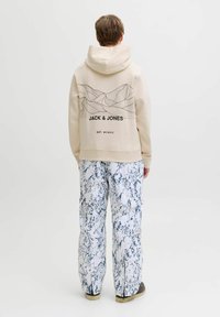 Haut à capuche beige avec un motif de ligne de montagne et un logo au dos, associé à un pantalon cargo marbré bleu et blanc. Casual, coupe décontractée.