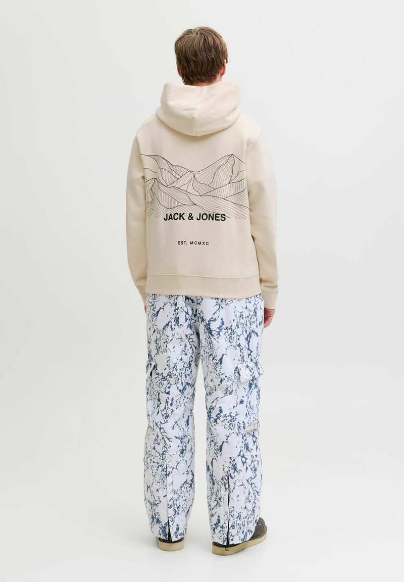 Haut à capuche beige avec un motif de ligne de montagne et un logo au dos, associé à un pantalon cargo marbré bleu et blanc. Casual, coupe décontractée.