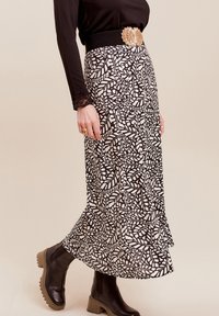 Schwarz-weiß gemusterter Midirock mit fließendem Design und strukturiertem Taillenbund. Getragen mit schwarzen Ankle Boots und einem dekorativen Gürtel.