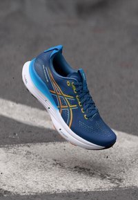 Baskets de course bleu avec texture en maille, ornées d'accents orange et jaune. Design léger et semelle rembourrée, idéales pour le confort et la performance.