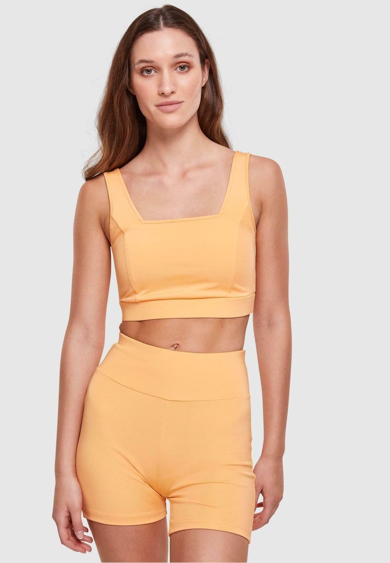 Orange kortärmad tanktopp med fyrkantig halsringning, i kombination med högmidjade shorts, båda i mjukt och stretchigt material.