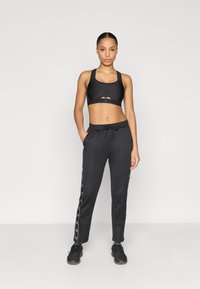 Μαύρο αθλητικό σουτιέν με σχέδιο με άνοιγμα, συνδυασμένο με μαύρο παντελόνι με πλαϊνές λεπτομέρειες. Το υλικό φαίνεται ελαστικό και εφαρμοστό, κατάλληλο για αθλητική χρήση.