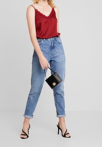 Rød satin top med blondekant, højtsiddende lyseblå denim jeans, sort struktureret håndtaske med guldfarvet hardware og sorte hæle sandaler.