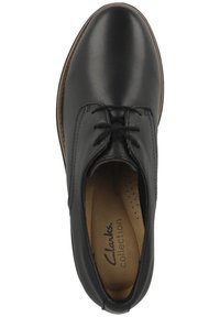 Musta nahkakenkä, jossa on sileä pinta, pyöreä kärki, nauhakiinnitys ja vaaleanruskea pohjallinen, jossa on teksti "Clarks Collection."