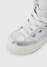 Sneaker bianco con punta e dettagli laterali argentati lucidi, lacci argentati texturizzati e suola di gomma bianca. Presenta una superficie liscia.