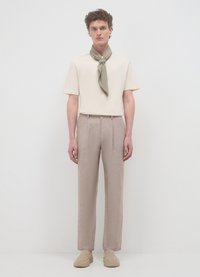 T-shirt beige a maniche corte, pantaloni grigi chiari e una sciarpa verde. I pantaloni hanno una finitura testurizzata; le scarpe sono slip-on beige.