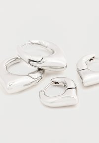 Neli läikivat hõbedast kõrvarõngast, millel on j äme ja veidi nurgeline disain, valgel pinnal.