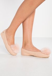Pletené pantofle v jemně růžové barvě s huňatými bambulkami vpředu, s plochým tkaným designem a zaoblenou špičkou.