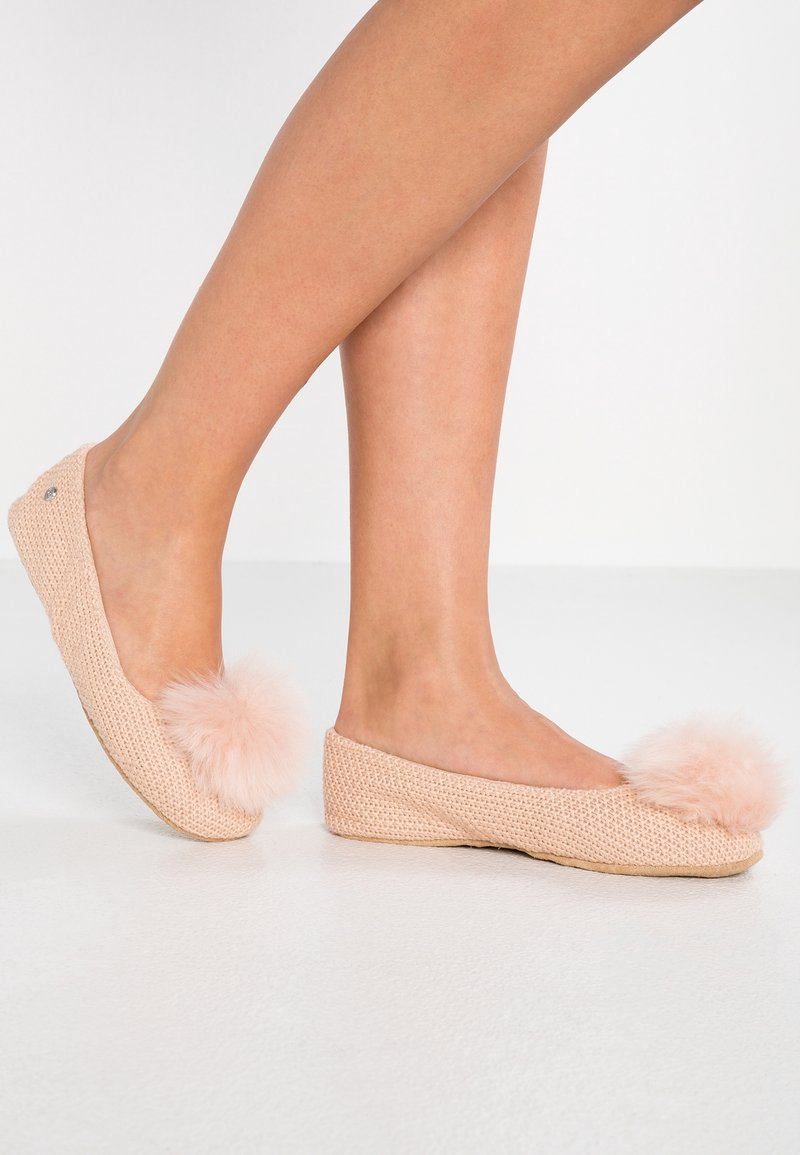 Pletené pantofle v jemně růžové barvě s huňatými bambulkami vpředu, s plochým tkaným designem a zaoblenou špičkou.