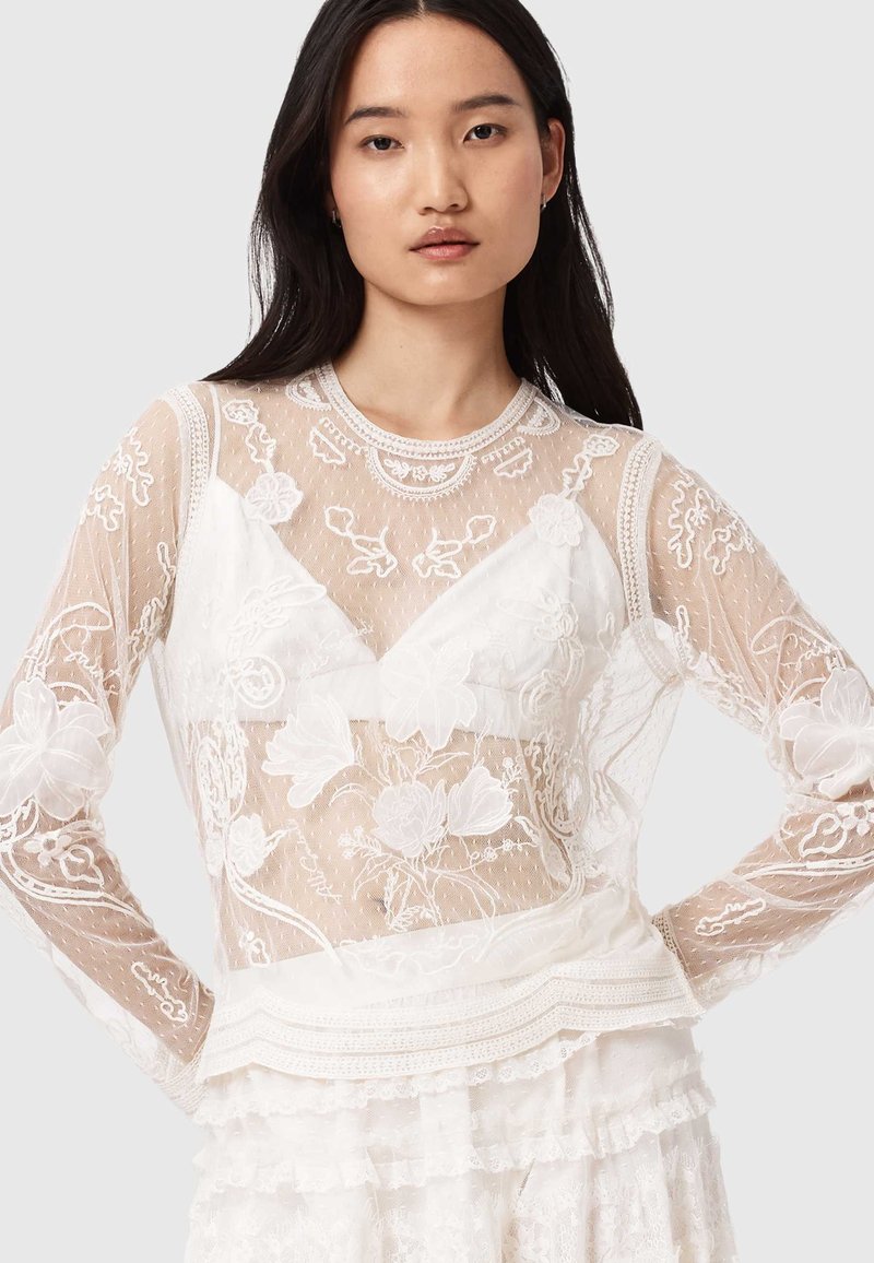 Durchsichtige weiße Langarmbluse mit floraler Stickerei, strukturiertem Overlay, runder Ausschnitt und Spitzenakzenten am Saum.