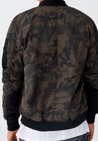 Veste bomber camouflage en vert et noir, dotée d'un col côtelé, de poignets élastiques et de poches zippées avec une texture lisse et brillante.