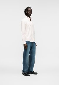 Chemise rose pâle à boutons avec col, associée à un jean denim bleu à jambes larges et des chaussures en cuir noir. Design net et épuré avec une texture douce.