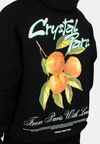 Felpa nera con un vivace grafico di pesche arancioni e foglie verdi, accompagnato dalla scritta bianca "Crystal Paris" e "From Paris With Love" sotto.