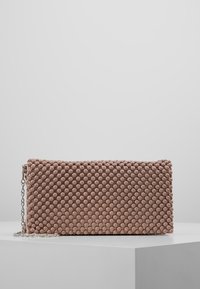 Pochette rectangulaire rose clair avec un motif en points en relief texturé et une chaîne argentée. Fermeture éclair sur un côté.