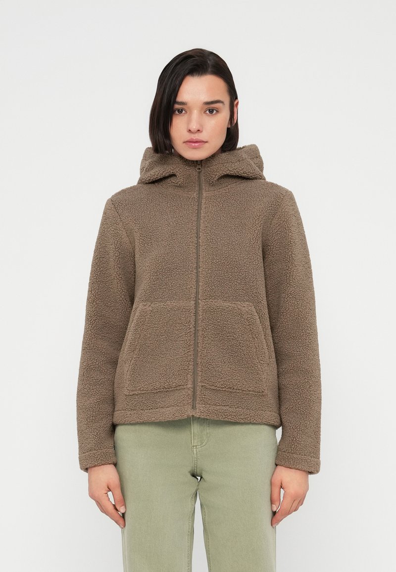 Καφέ μάλλινο μπουφάν με κουκούλα, μπροστινό φερμουάρ και δύο μεγάλες τσέπες. Το υλικό είναι υφή με απαλό, ζεστό ύφος.