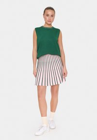 Débardeur sans manches vert en tricot avec encolure blanche, associé à une jupe rose avec des rayures verticales vertes et un ourlet évasé. Baskets blanches portées.