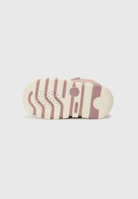 Semelle de sneaker rose et crème avec des rayures courbées, des motifs circulaires et des trous de ventilation. Matériau en caoutchouc durable avec une texture antidérapante.