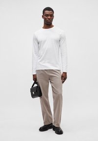 Balta ilgomis rankovėmis marškiniai, kreminės kelnės, juoda rankinė ir juodi batai. Apranga pasižymi paprastu dizainu su lygiais paviršiais.