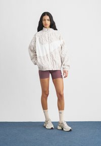 Ελαφρύ μπουφάν με λεοπάρ μοτίβο σε μπεζ, λευκό φερμουάρ μπροστά και ψηλό γιακά. Συνδυασμένο με βερμούδα μπορντό. Αθλητικά παπούτσια και κρεμ κάλτσες.