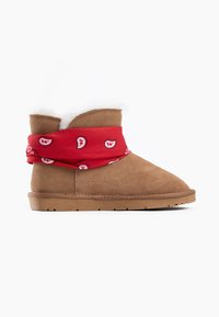 Stivale alla caviglia in suede tan con una fodera in pelliccia bianca e una fascia rossa decorata con motivi bianchi. Suola piatta in gomma con dettagli testurizzati.