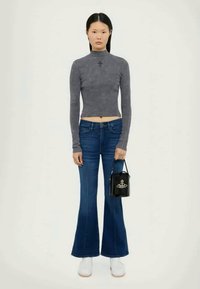 Camisola cinza de manga longa cropped com bordados decorativos, jeans azul de boca de sino, sapatilhas brancas e uma pequena mala preta com um logótipo.