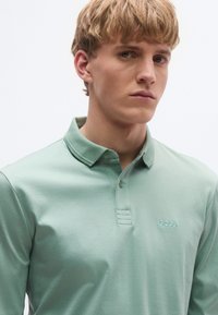 Világoszöld galléros póló, galléros nyakkivágással, két gombbal és a bal mellrészen egy kis "BOSS" hímzett logóval. Simas textúra.