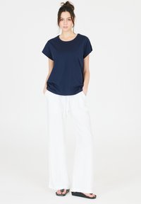 Marinblå t-shirt med kort ärm som kombineras med vita vida byxor. Byxorna har dragsko och en avslappnad passform. Svarta flip-flops fulländar looken.