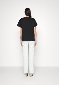 T-shirt en coton noir à manches courtes, associé à un pantalon large blanc. Le modèle porte des talons noirs avec des accents dorés.