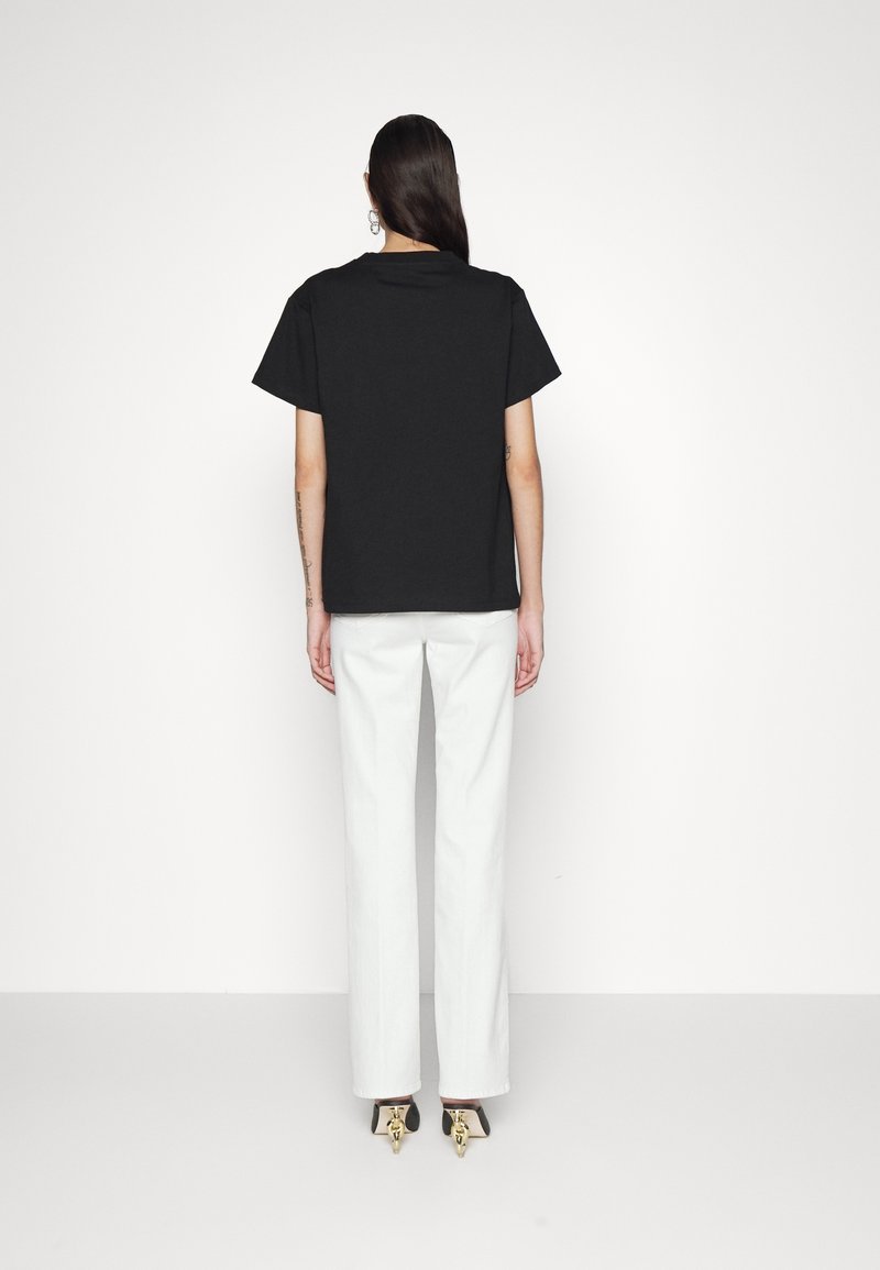 T-shirt en coton noir à manches courtes, associé à un pantalon large blanc. Le modèle porte des talons noirs avec des accents dorés.