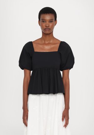 Musta puffi hiha -pusero, jossa on neliönmuotoinen pääntie, plissee-bodice ja sileä tekstuuri, yhdistettynä valkoiseen brodeerattuun hameeseen.