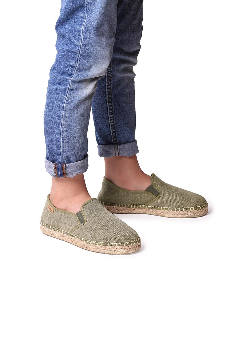 Gröna canvas slip-on skor med flätade jutesulor, featuring elastiska sidopaneler och en texturerad yta. Bärs med uppvikta denimjeans.