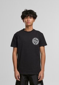 T-shirt en coton noir à manches courtes, col rond, avec un graphique circulaire blanc sur la poitrine gauche avec un design animal et du texte.
