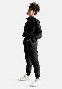 Giacca a vento nera con colletto alto e tasche con zip, abbinata a pantaloni jogger coordinati con cintura elastica e polsini.