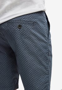 Námorně modré šortky s jemným bílým opakujícím se vzorem, přední zapínání na knoflík a boční kapsy. Vyrobeno z lehkého materiálu.