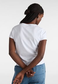 Hvid kortærmet t-shirt, bomuldsmateriale, tætsiddende design, rund halsudskæring, glat tekstur, båret med blå denim jeans, set bagfra.