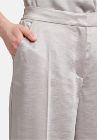 Ljusgrå linnebyxor med en slät textur, utrustade med snedställda sidofickor och en platt framsida. Tyget faller mjukt.