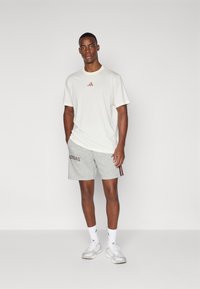 Világos bézs póló, kis bordó logóval, szürke rövidnadrággal, az oldalvonalak bordó "ADIDAS" felirattal. Fehér sportcipő.