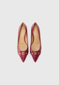 Pump in pelle bordeaux con tacco alto, punta affusolata, dettagli in metallo dorato e una texture liscia. L'interno è foderato e presenta il logo del marchio.
